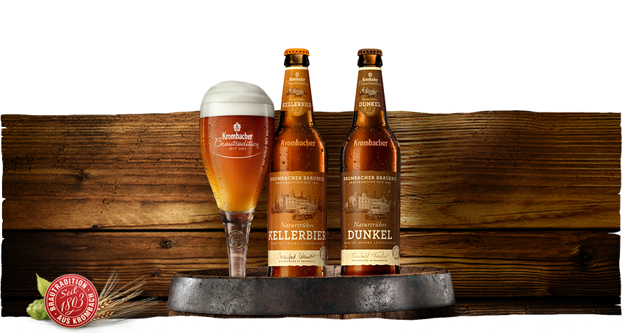 Zwei Flaschen 'Kellerbier Dunkel' und ein Glas mit dunklem Bier stehen auf einem rustikalen Holzbrett. Die Flaschen sind mit dem Logo von 'Krombacher' versehen.