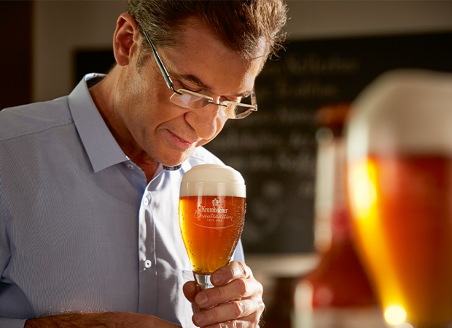 Ein Mann hält ein Glas Bier mit einer dichten Schaumkrone. 