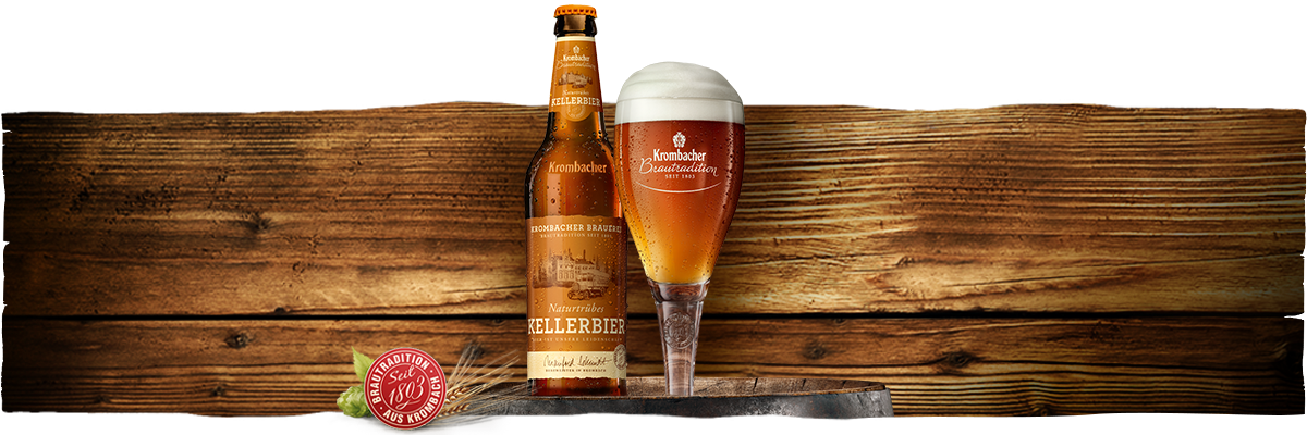 Eine Flasche Krombacher Kellerbier steht neben einem Glas mit schaumigem Bier. Im Hintergrund sind Holztexturen sichtbar.