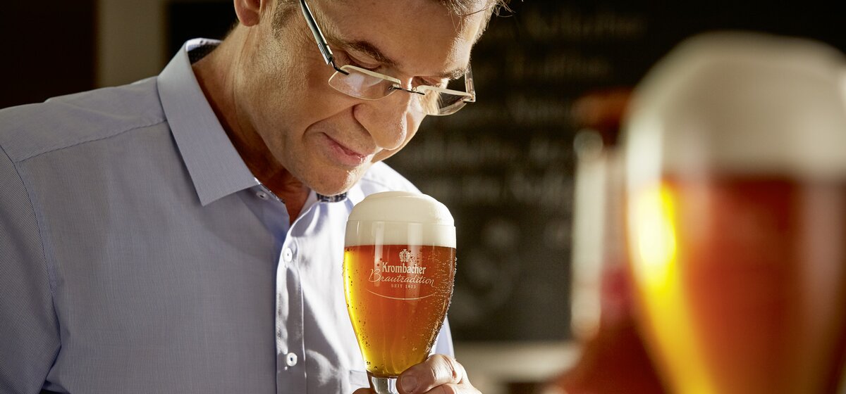 Ein Mann hält ein Glas Kellerbier mit Schaumkrone in der Hand. 